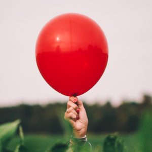 Woman holding single red balloon.